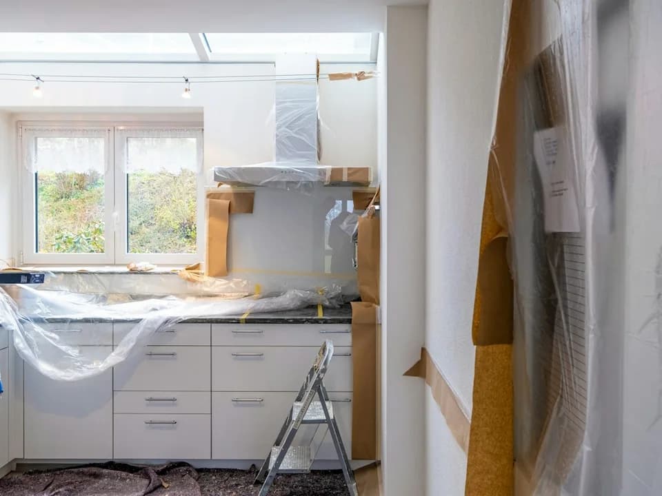 A kitchen with unfinished work, covered cabinets and a ladder
